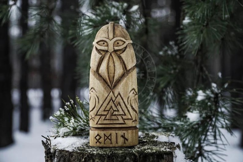 Puede incluir: Una talla de madera de un dios n&oacute;rdico con casco y barba. La talla est&aacute; decorada con un s&iacute;mbolo Valknut y la palabra "Odin" en runas.