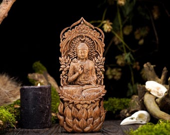 May include: A detailed wooden Buddha statue, carved with intricate details, seated on a lotus flower base. The statue features a halo and is surrounded by floral elements. A dark candle and natural elements are in the background.