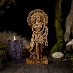 May include: A wooden statue of the Roman goddess Diana, standing with a bow and arrow. The statue is carved with intricate details and has a natural wood finish. The base of the statue is inscribed with the word "Diana".