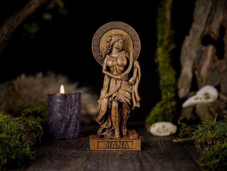 May include: A wooden statue of the Roman goddess Diana, standing with a bow and arrow. The statue is carved with intricate details and has a natural wood finish. The base of the statue is inscribed with the word "Diana".