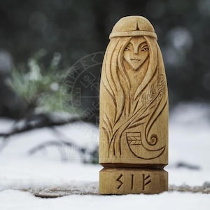 Puede incluir: Una talla de madera de una diosa n&oacute;rdica con el pelo largo y un tocado. La talla est&aacute; detallada con una planta y un s&iacute;mbolo de runa, "Sif", en la base.