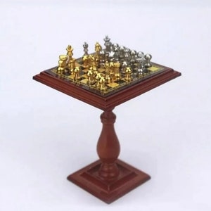 May include: Miniature chess set with gold and silver pieces on a wooden board. The board is set on a small, dark brown wooden table with a square base and a turned pedestal.