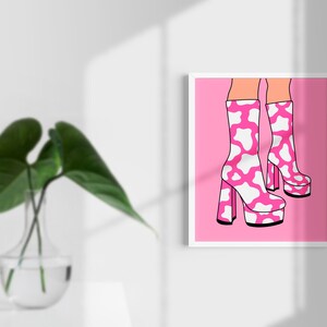 May include: A pair of pink platform boots with a white cow print design. The boots are on a pink background.