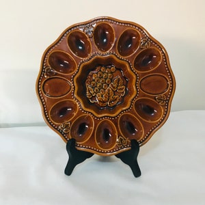 May include: A handmade wooden sign with the text "Welcome to our home" in a handwritten style. The sign is painted white with a dark stained wooden frame. A small green plant is placed on the sign.