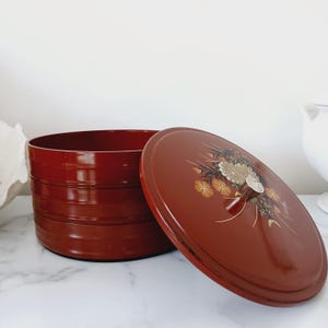 May include: A red tiered storage box with a floral design on the lid. The box is made of lacquered wood and has a traditional Japanese style.