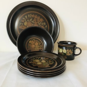May include: A set of brown stoneware dinnerware with a floral design in gold and brown. The set includes a large dinner plate, a smaller plate, a bowl, and a mug.