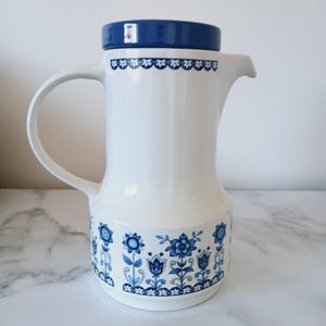 May include: A white ceramic coffee pot with a blue lid and floral pattern. The pot has a blue and white floral design around the bottom.