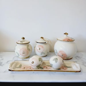 May include: A white ceramic kitchen set with a floral design in pink and green. The set includes three lidded jars, two salt and pepper shakers, and a rectangular serving tray with a gold trim.