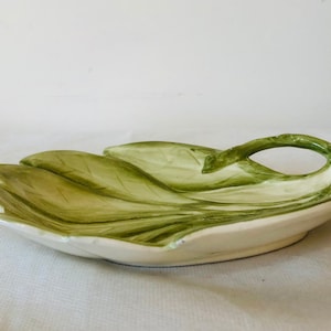 May include: A white ceramic serving dish shaped like a leaf with a green leaf design and a handle.