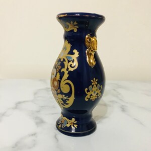 May include: A small, cobalt blue ceramic vase with gold accents and floral designs. The vase has a single handle on one side.