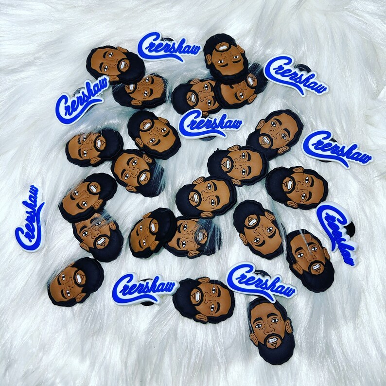 May include: A collection of shoe charms featuring a cartoon face with a beard and dark hair. The charms are brown, black, and tan. The word "Crenshaw" is written in blue script on some charms.