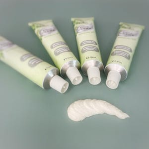 Könnte beinhalten: Vier Cremetuben mit grün-weißen Etiketten und ein Klecks Creme auf einer türkisfarbenen Oberfläche. Die Tuben haben silberne Kappen und sind mit Texten wie "Vitamin B5" und "Rosmarin & Mineral" beschriftet.