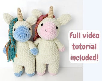 Puede incluir: Dos juguetes de unicornio de crochet, uno con una melena azul y blanca y el otro con una melena rosa y blanca. Ambos unicornios tienen cuerpos blancos y están de pie sobre una superficie blanca. El texto "¡Tutorial completo en video incluido!" está en el fondo.