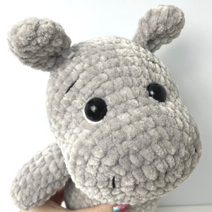 May include: A grey crocheted plush hippopotamus toy with black eyes. The hippopotamus has a textured, fuzzy surface.