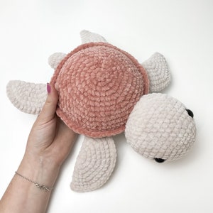 Pu&ograve; includere: Un giocattolo di tartaruga all'uncinetto con un guscio rosa e arti bianchi. La tartaruga ha occhi neri e una superficie morbida e testurizzata.