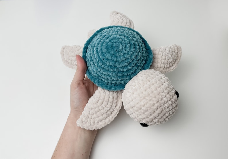 May include: A crocheted plush toy turtle with a teal shell and cream colored body and limbs.