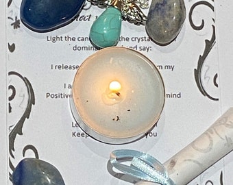 May include: A white candle with a blue ribbon tied around a rolled up piece of paper. There are several blue and green stones and a silver necklace with a turquoise pendant.