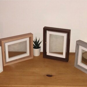 May include: Four different picture frames with white mats and various wood finishes. The frames are arranged on a wooden surface.