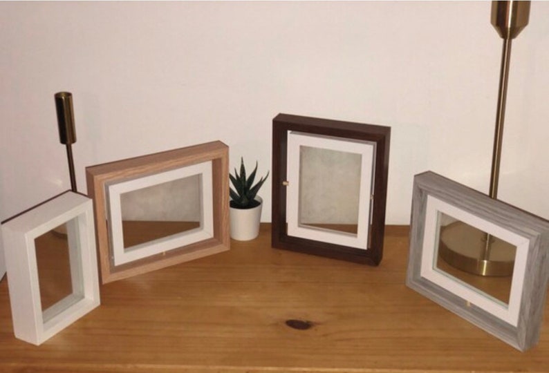 May include: Four different picture frames with white mats and various wood finishes. The frames are arranged on a wooden surface.