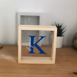 May include: A wooden frame with a clear acrylic insert featuring a blue letter K and the word "your" in white script.