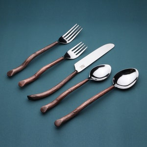 May include: Four pieces of copper-toned flatware with stainless steel heads. The set includes a fork, a knife, a spoon, and a larger spoon. The flatware is arranged on a blue background.