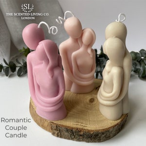 Puede incluir: Varias velas rom&aacute;nticas de pareja en tonos rosa y beige, presentadas sobre una rodaja de madera. Las velas representan figuras abrazadas, con mechas visibles. El texto "Romantic Couple Candle" est&aacute; en la parte inferior.