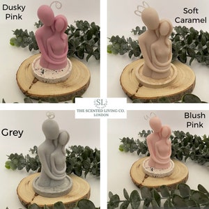 Puede incluir: Cuatro velas perfumadas en diferentes colores: rosa oscuro, caramelo suave, gris y rosa rubor. Cada vela representa una pareja abraz&aacute;ndose, sobre una base de hormig&oacute;n y una rodaja de madera. Las velas tienen un dise&ntilde;o de halo y est&aacute;n rodeadas de vegetaci&oacute;n.