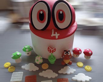 Może przedstawiać: Czerwono-biały tort ozdobiony postacią z gry wideo Super Mario Bros. Tort jest otoczony różnymi dekoracjami, w tym grzybami, monetami i cegłami.
