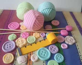 Könnte beinhalten: Ein Set aus pastellfarbenen Garnknäueln, Knöpfen und einem Lineal, alles aus Fondant. Die Garnknäuel sind rosa, hellblau und hellgrün. Die Knöpfe sind in verschiedenen Farben, darunter rosa, blau, grün, gelb und lila. Das Lineal ist gelb mit schwarzen Markierungen.