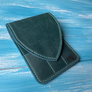 May include: A dark green leather wallet with a flap closure and a stitched design. The wallet has a pocket on the front and the initials "TK" are embossed on the back.