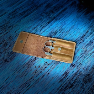 May include: A brown leather case with a snap closure, containing a pair of nail clippers and a nail file.