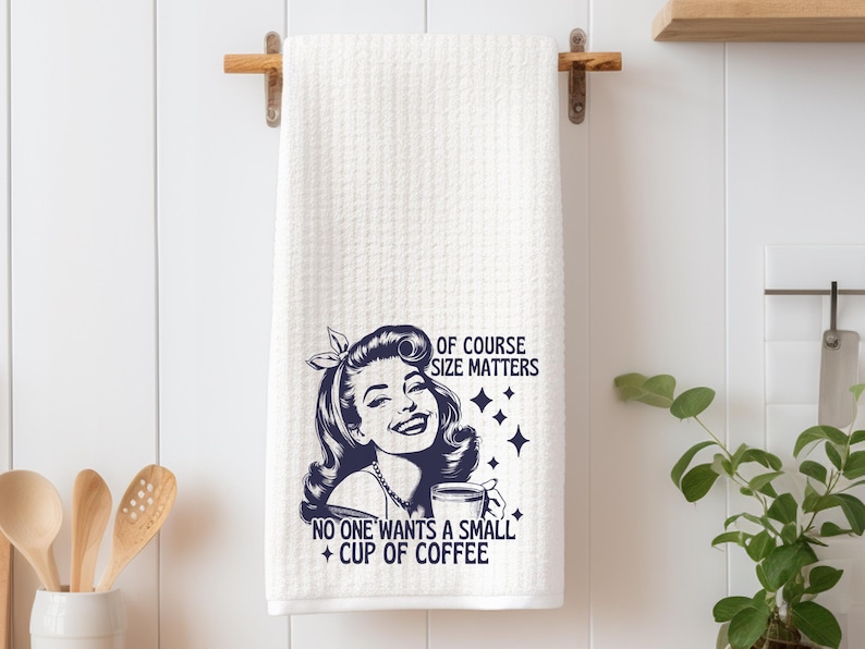 May include: White kitchen towel with a black and white illustration of a woman holding a coffee mug. The text reads "Of course size matters. No one wants a small cup of coffee."