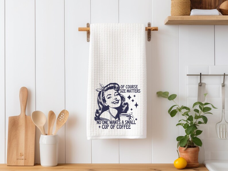 May include: White kitchen towel with a blue graphic of a woman holding a cup of coffee. The text reads "Of course size matters. No one wants a small cup of coffee."