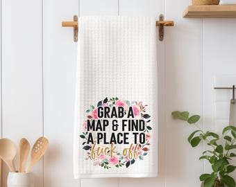 May include: White kitchen towel with a floral design and the text "Grab a map & find a place to f*** off" in black and gold lettering.