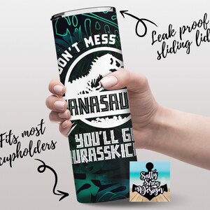 Puede incluir: Un vaso de acero inoxidable verde y negro con un gr&aacute;fico de dinosaurio y el texto "Don't Mess with a  Anasaurus You'll Get Urasskiched". El vaso tiene una tapa deslizante a prueba de fugas y se adapta a la mayor&iacute;a de los portavasos.