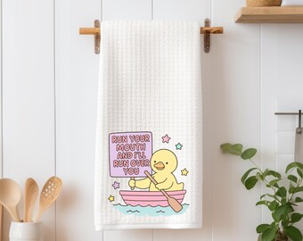 May include: White waffle-weave kitchen towel with a cartoon duck in a pink boat, holding a sign that reads "Run Your Mouth and I'll Run Over You." The design includes stars and water waves.