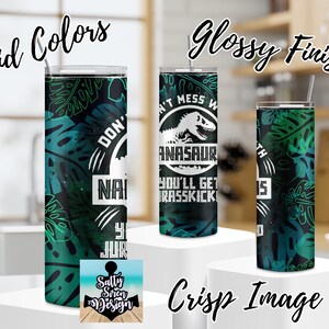 Puede incluir: Tres vasos de acero inoxidable con acabado brillante. Los vasos presentan un dise&ntilde;o verde y negro con un gr&aacute;fico de dinosaurio y el texto "No te metas con un dinosaurio, te dar&aacute;n una patada en el c&eacute;sped".