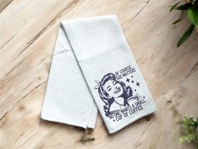May include: White kitchen towel with a blue graphic of a woman holding a cup of coffee. The text reads "Of course size matters. No one wants a small cup of coffee."