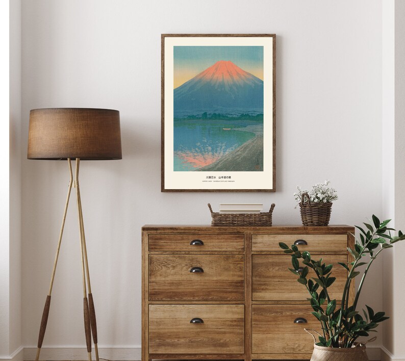 May include: A framed print of a Japanese landscape featuring Mount Fuji. The artwork depicts the mountain with a red-orange peak, set against a blue sky and water. The print is in a wooden frame and hangs above a wooden dresser.