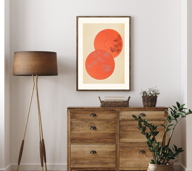 May include: A framed print of a minimalist abstract art piece featuring two overlapping circles in shades of orange and white with a pattern of small white dots. The print is displayed on a wall above a wooden dresser.