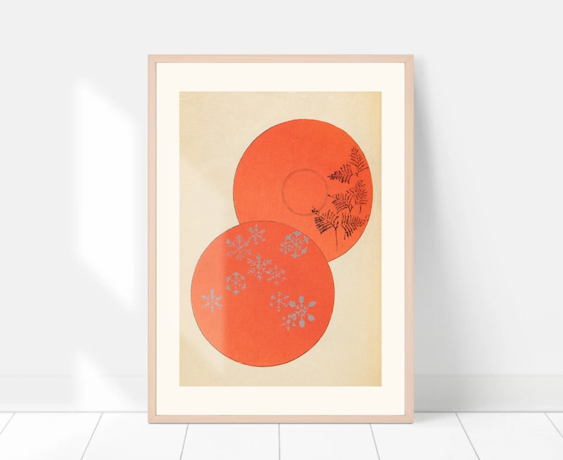 May include: Two orange circular plates with a white background. The top plate has a black fern design and the bottom plate has a silver snowflake design.