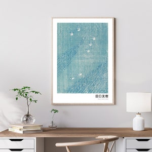 May include: A framed print of a blue and white abstract design with the Japanese text "田口友樹" at the bottom. The print is in a light wood frame and is hanging on a white wall.