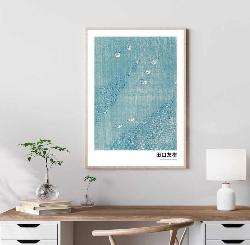 May include: A framed print of a blue and white abstract design with the Japanese text "田口友樹" at the bottom. The print is in a light wood frame and is hanging on a white wall.