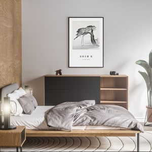 May include: A bedroom interior with a wooden bed frame, a grey duvet, and a black bedside table with a lamp. A framed black and white print of a tree hangs on the wall above a black and wood cabinet with shelves. A potted plant is in the corner of the room.