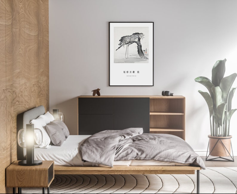 May include: A bedroom interior with a wooden bed frame, a grey duvet, and a black bedside table with a lamp. A framed black and white print of a tree hangs on the wall above a black and wood cabinet with shelves. A potted plant is in the corner of the room.