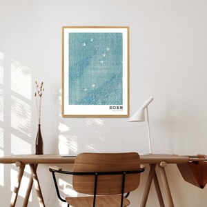 May include: A framed print of a blue and white abstract design with the text "日本画" in the bottom right corner. The print is hanging on a white wall above a wooden desk with a chair.