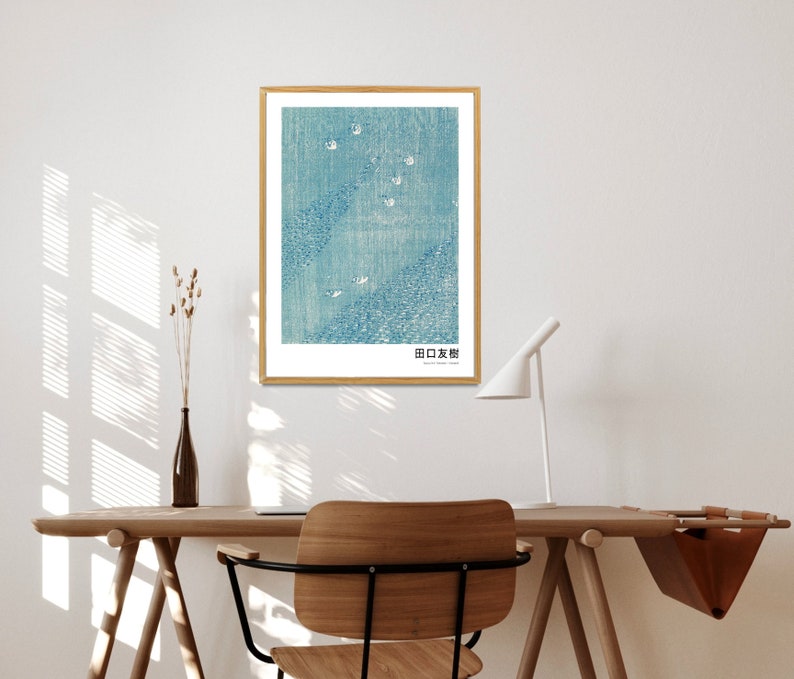 May include: A framed print of a blue and white abstract design with the text "日本画" in the bottom right corner. The print is hanging on a white wall above a wooden desk with a chair.