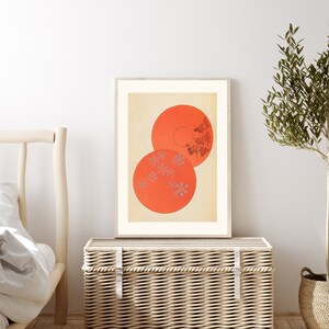 May include: A framed print of a minimalist abstract art piece featuring two overlapping circles in shades of orange with a pattern of small grey flowers inside.