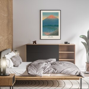 May include: A framed art print depicting a Japanese landscape with a mountain and water. The mountain has a red and orange peak, with the text "Fuji Japan" at the bottom. The print is displayed in a bedroom setting.