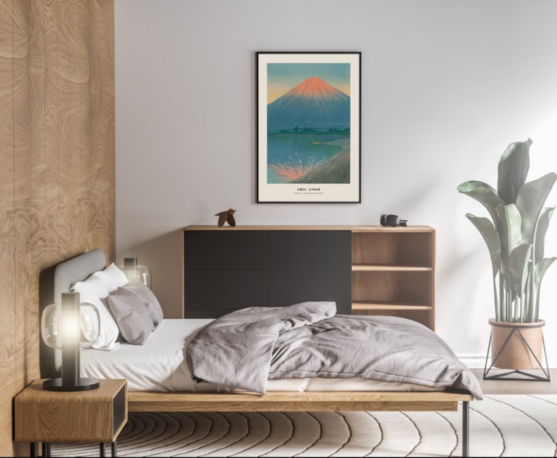 May include: A framed art print depicting a Japanese landscape with a mountain and water. The mountain has a red and orange peak, with the text "Fuji Japan" at the bottom. The print is displayed in a bedroom setting.